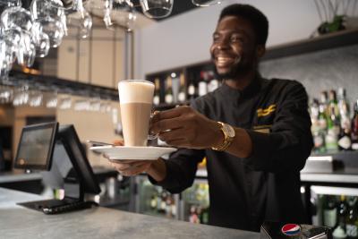 A man in uniform stood behind a bar holding a coffee